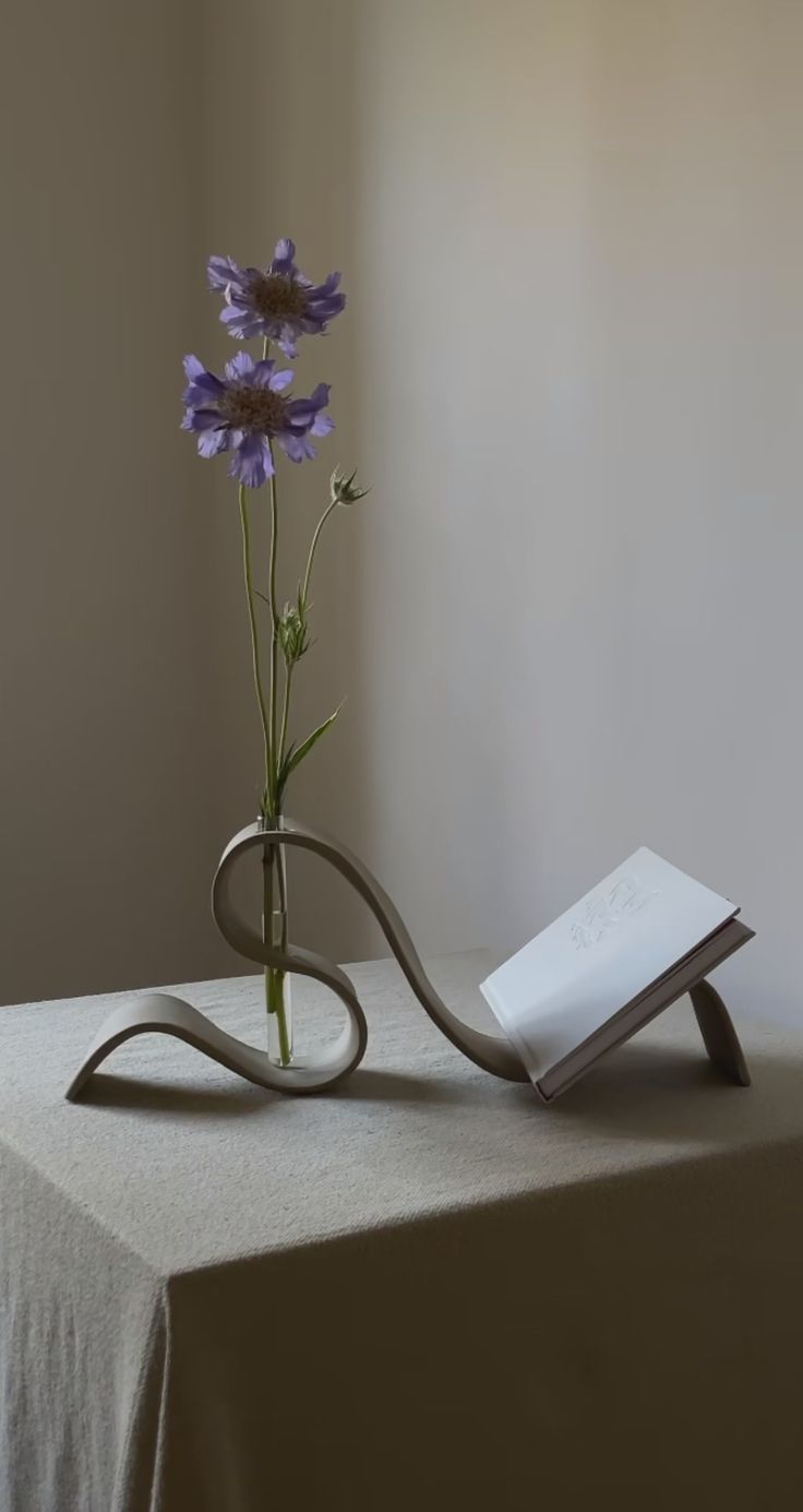 a vase with flowers in it sitting on a table next to a book and a pen