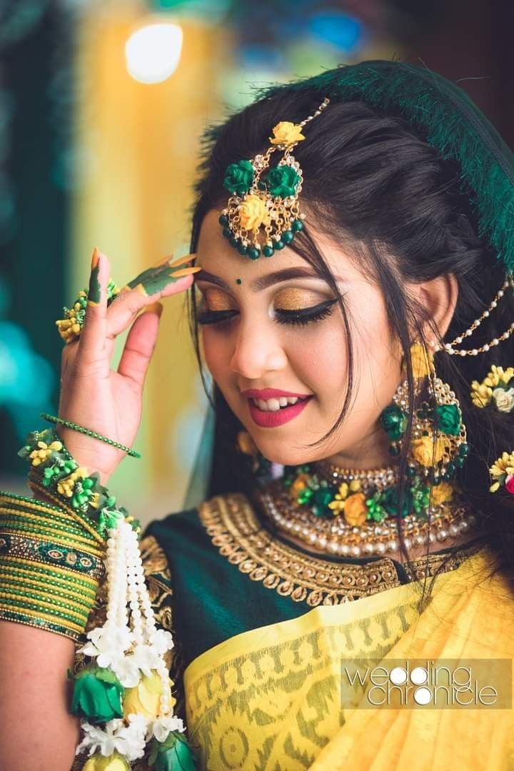 a woman in green and yellow sari with jewelry on her head, looking at the camera