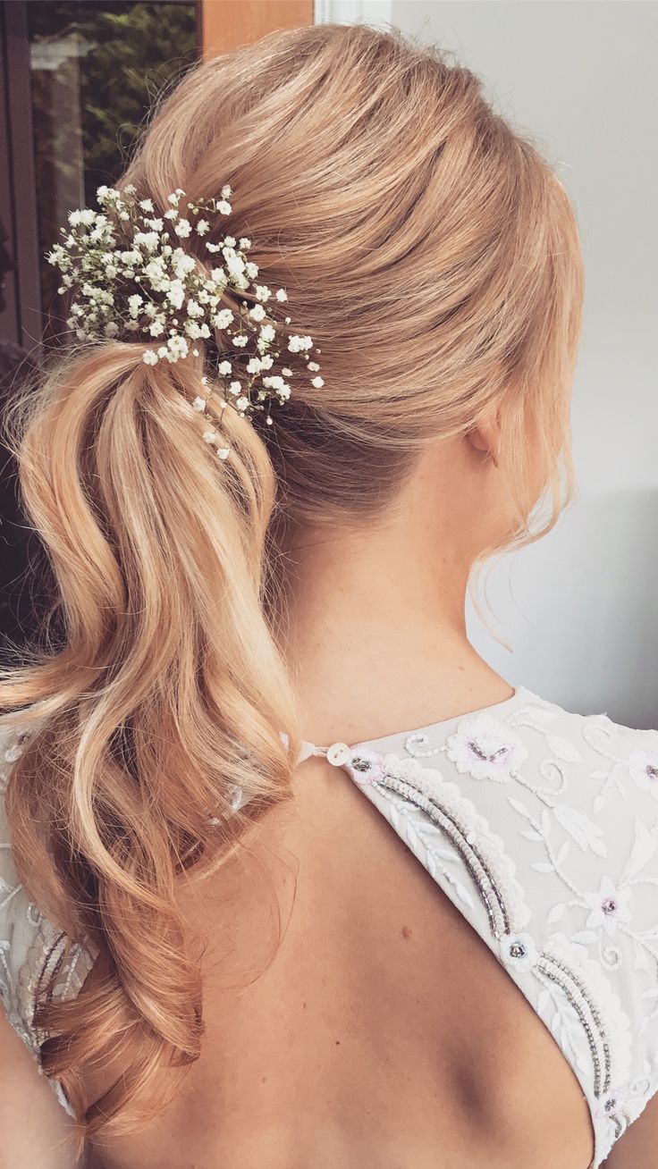 a woman sitting at a table with her hair in a low ponytail and flowers in her hair