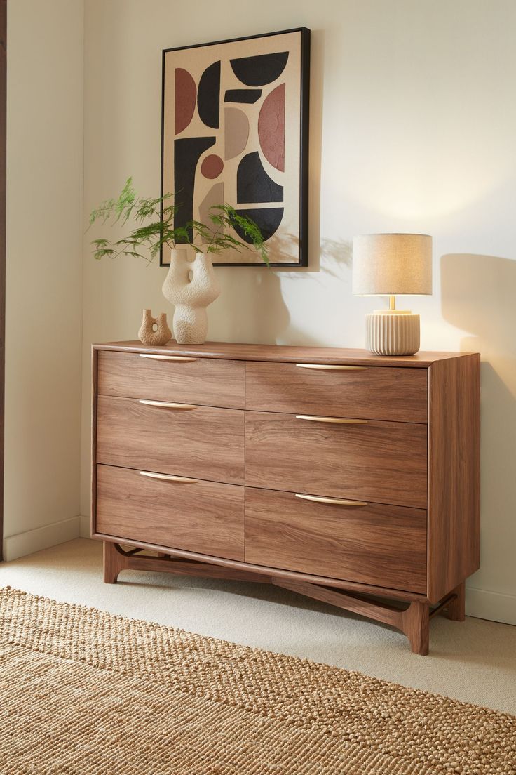 a wooden dresser sitting in a room next to a lamp and painting on the wall