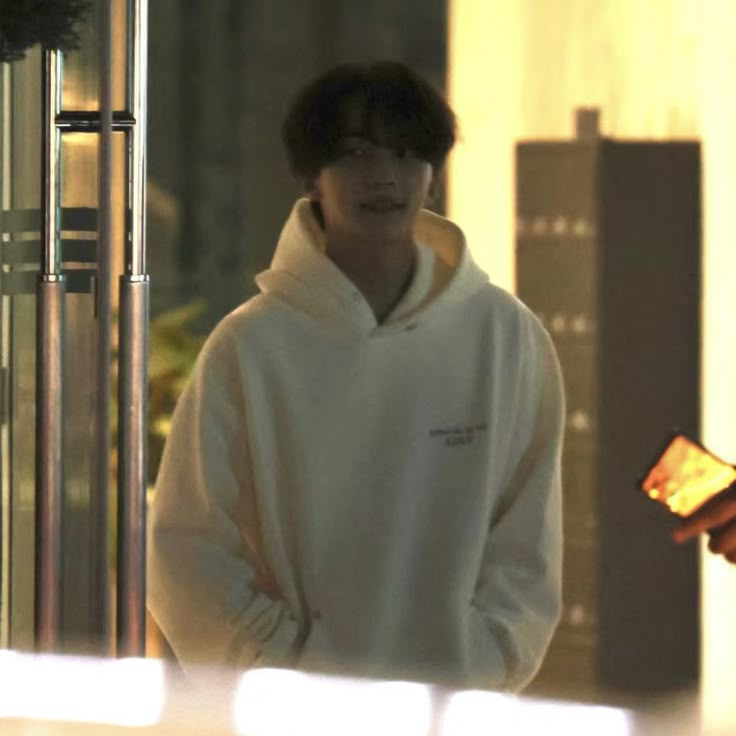 a man in a white hoodie standing next to a building