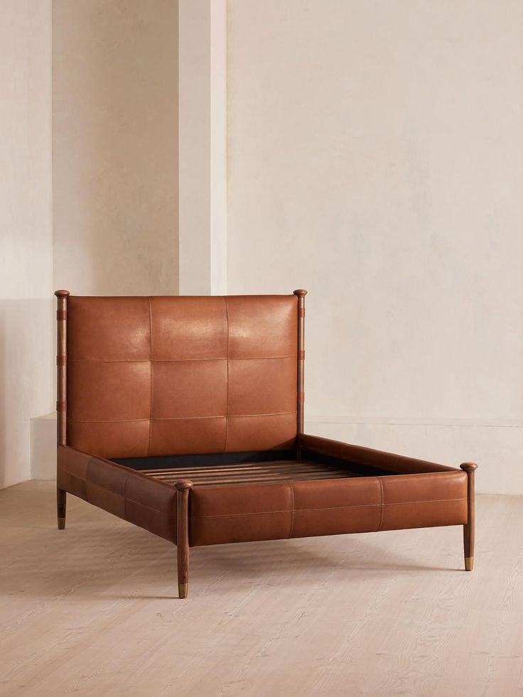 a brown leather bed frame sitting on top of a wooden floor next to a white wall