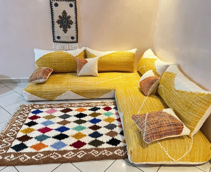 a living room with yellow couches and rugs on the floor in front of a white wall