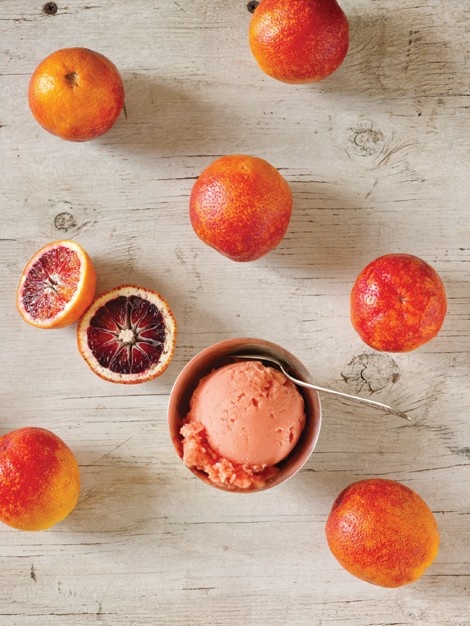 oranges and grapefruit on a wooden table with a bowl of ice cream