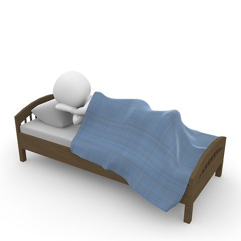 a small white person laying in a bed with a blue blanket on top of it