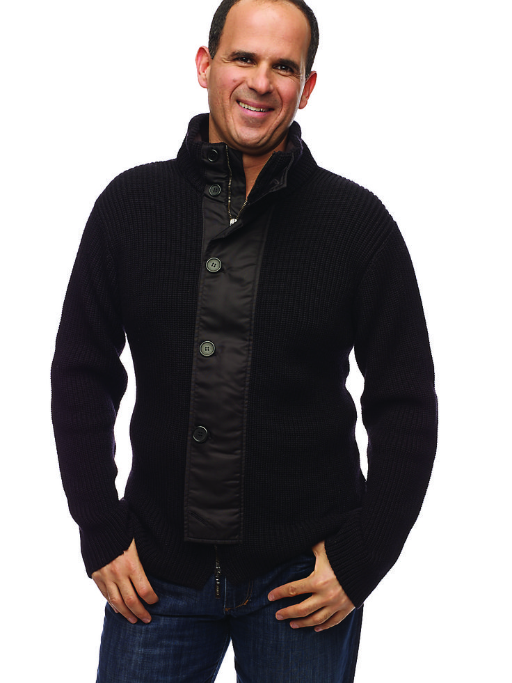 a man standing with his hands in his pockets and smiling at the camera while wearing a black jacket