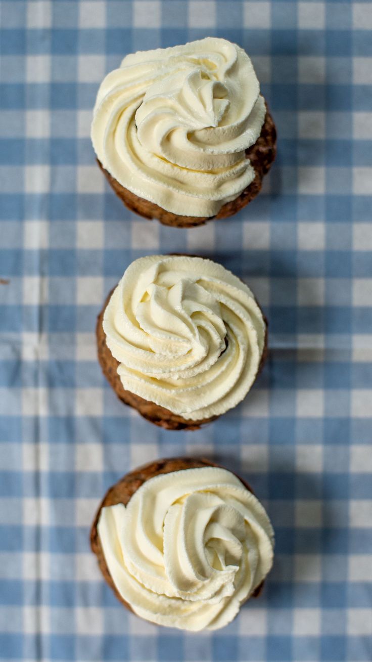 three cupcakes with white frosting sitting on a blue and white checkered table cloth