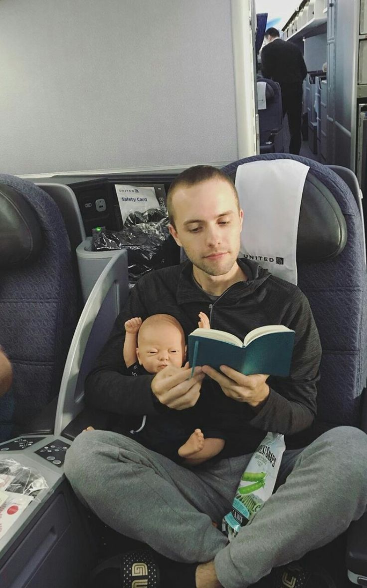 a man sitting on an airplane reading a book to a small baby in his lap