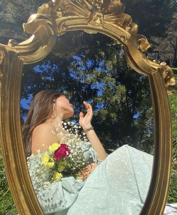 a woman sitting on the ground in front of a mirror holding a bouquet of flowers