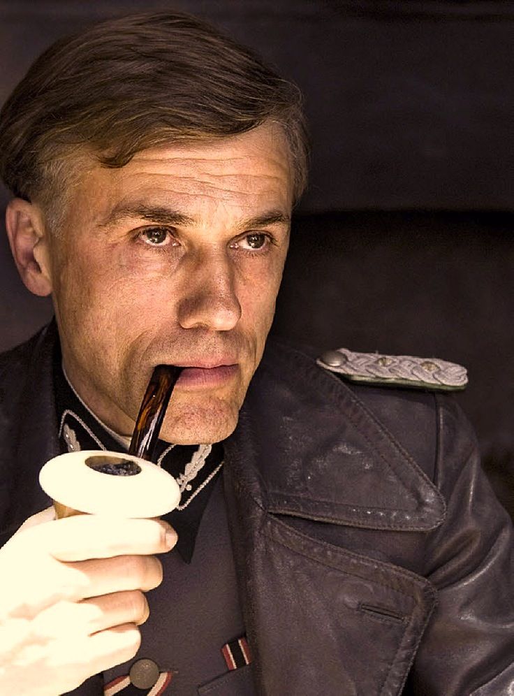 a man with a pipe in his mouth wearing a leather jacket and holding a remote control