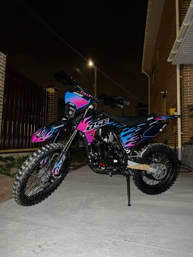 a pink and blue dirt bike parked in front of a building