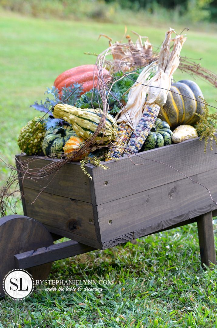 a wooden wheelbarrow filled with assorted vegetables and plants in the middle of a grassy field