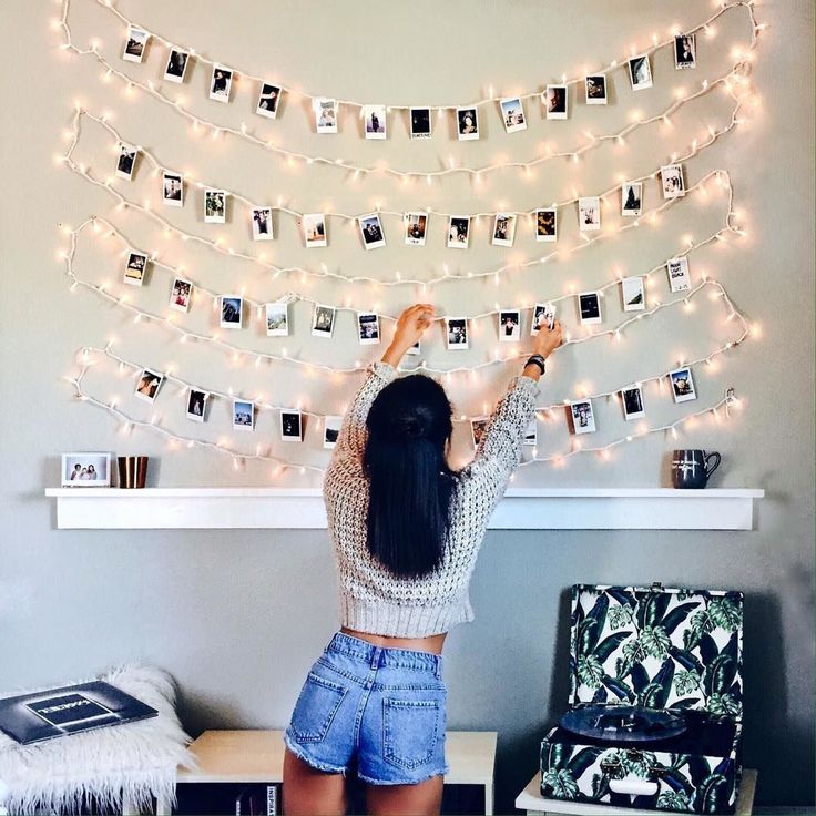 a woman standing in front of a wall with pictures and lights hanging from it's sides