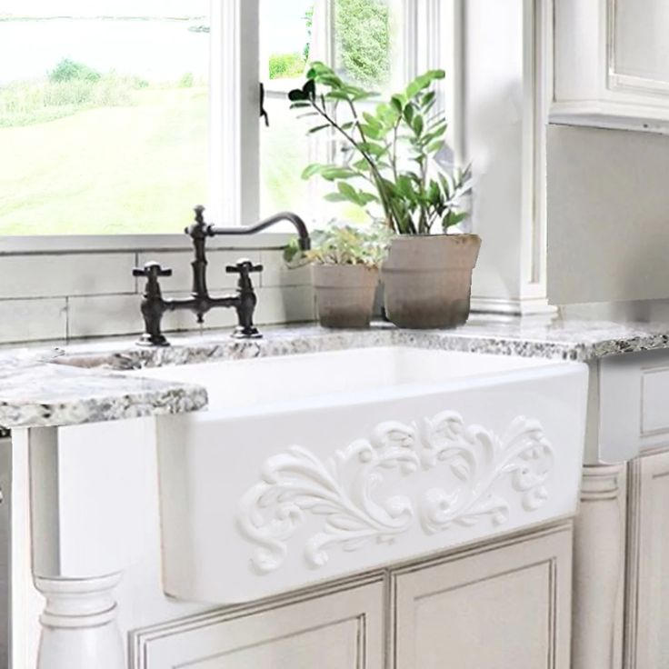 a white kitchen sink sitting under a window next to a potted plant on top of a counter