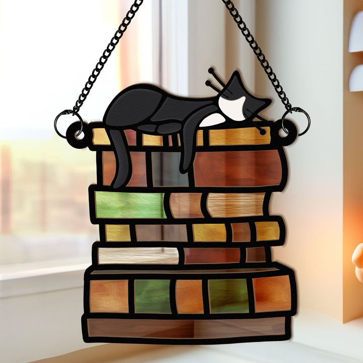 a stained glass cat sleeping on top of a stack of books hanging from a chain