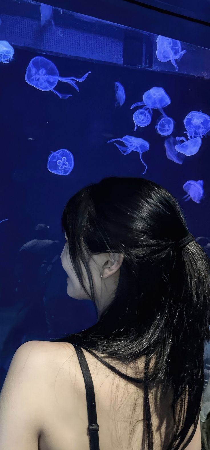 a woman standing in front of an aquarium looking at some jelly fish swimming around her