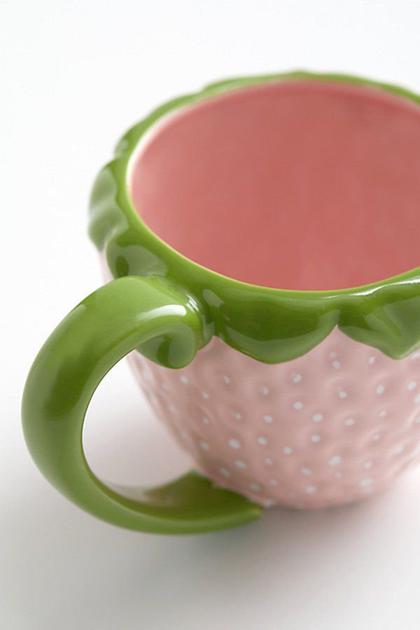 a green and pink coffee cup sitting on top of a white table