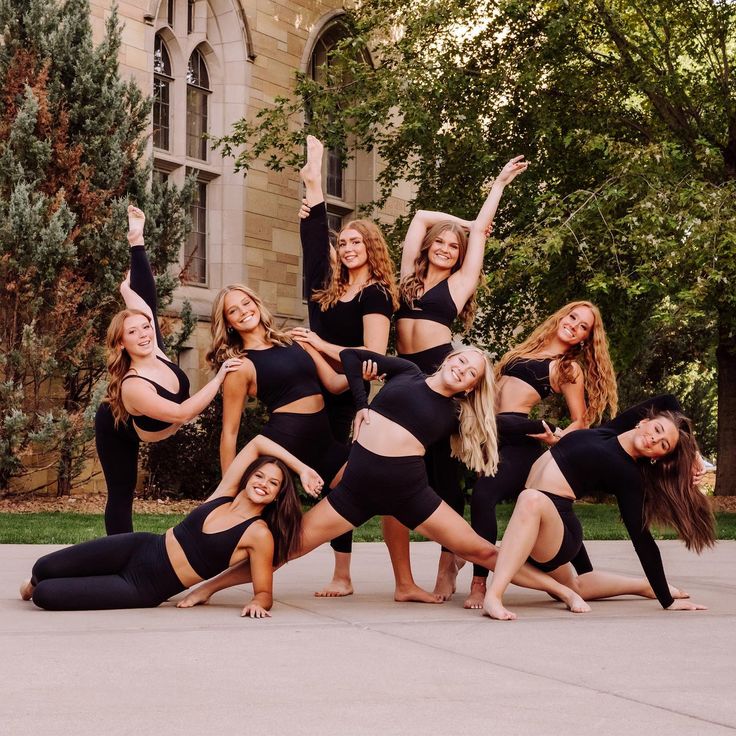 a group of young women in black outfits posing for a photo on the sidewalk with their arms up