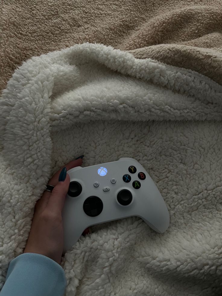 a person is holding a controller for a video game system on a bed covered in a blanket