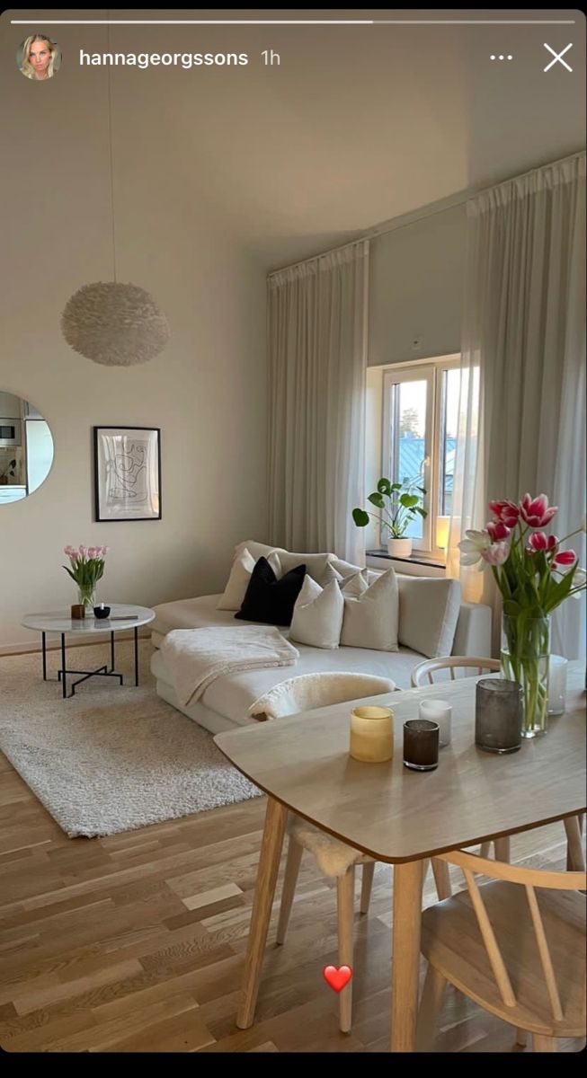 a living room filled with furniture and flowers on top of a wooden table in front of a window