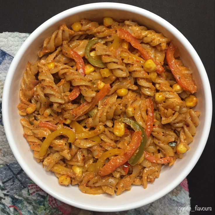 a white bowl filled with pasta and vegetables on top of a colorful table cloth next to a fork