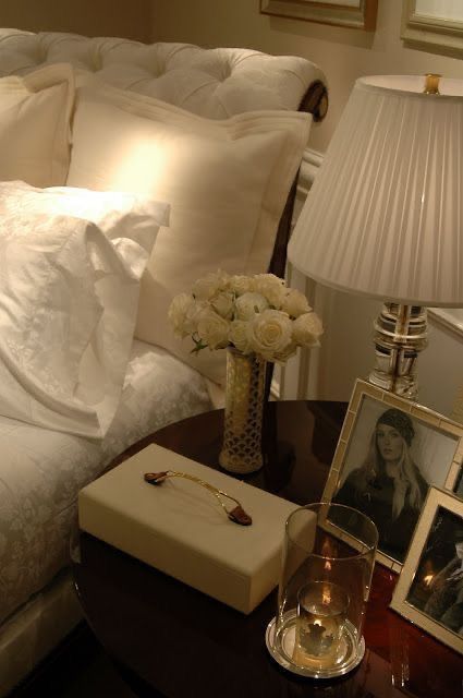 a bed with white pillows and pictures on the side table next to it, along with a vase filled with flowers