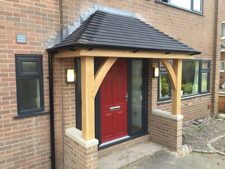 a red door is in front of a brick building with a black roof and wooden frame