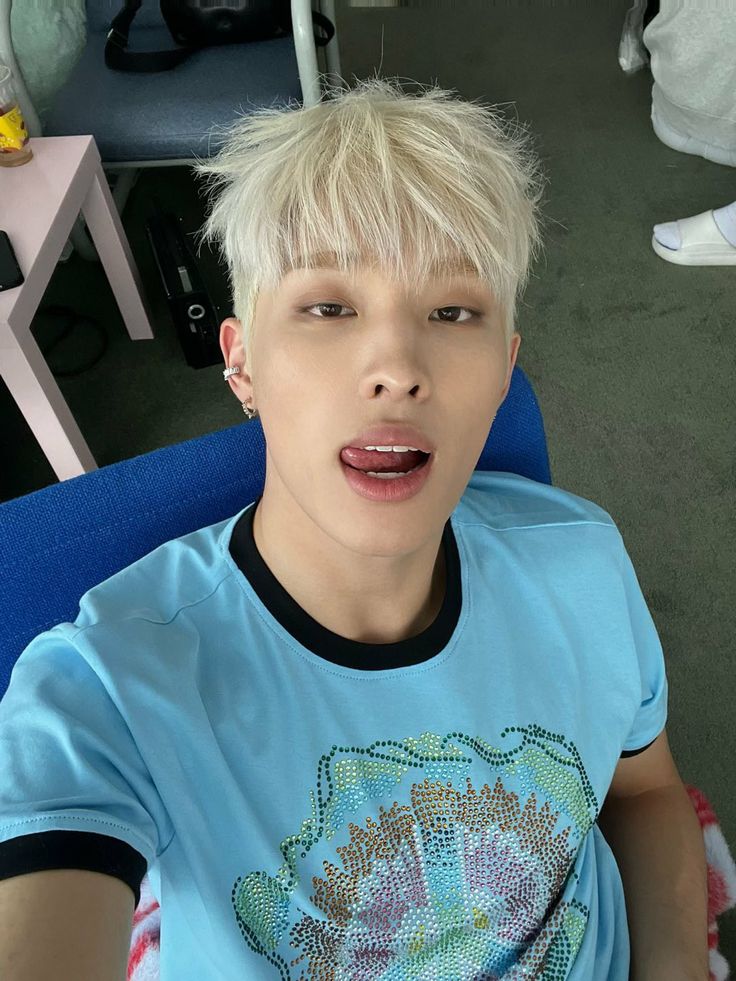 a young man with blonde hair sitting in a blue chair and making a funny face