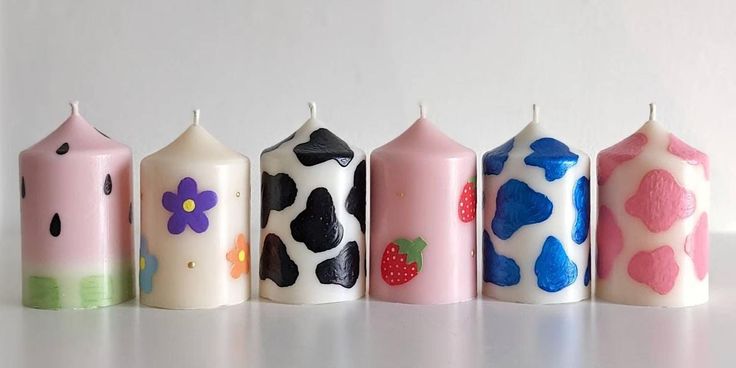 five candles are lined up in the shape of cows and strawberrys, with different designs on them