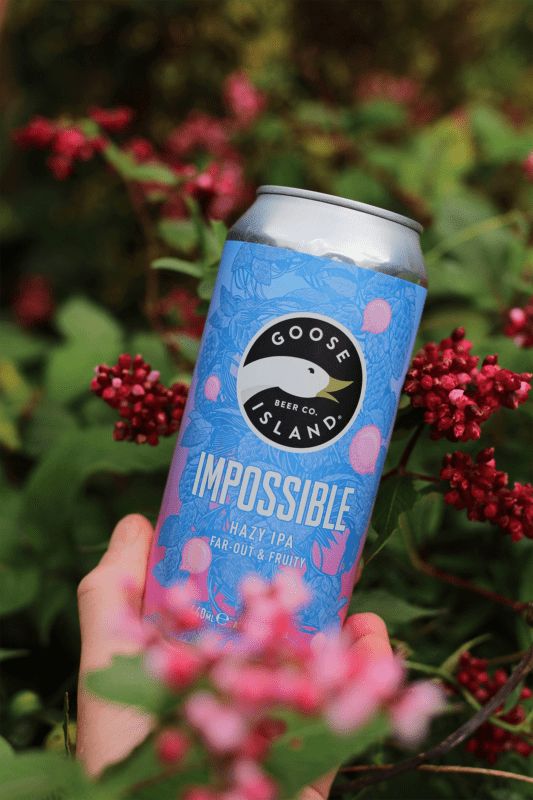 someone holding up a can of impossibleible beer in front of some pink flowers and green leaves