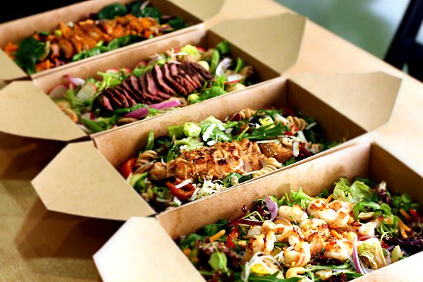 three boxes filled with different types of salads on top of a wooden table next to each other