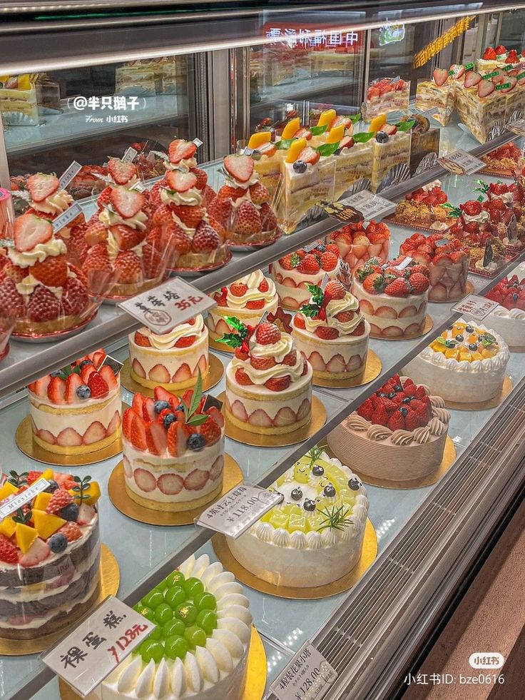 there are many different cakes on display in the glass case at this store, including strawberries and other desserts