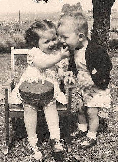 two young children sitting on top of a wooden chair next to a tree in the grass