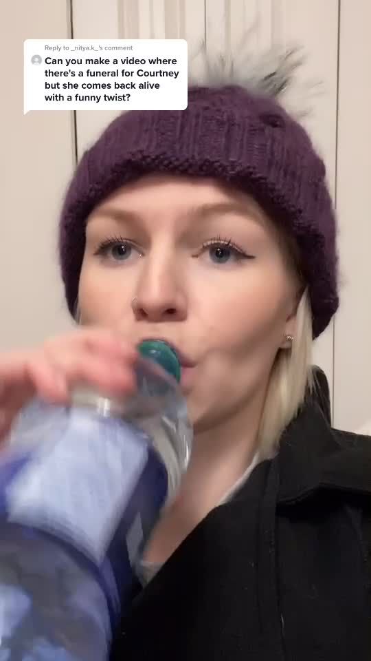 a woman drinking from a water bottle while wearing a knitted hat and black jacket