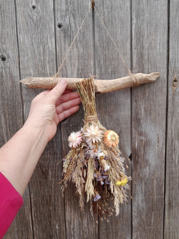 a hand holding a stick with dried flowers hanging from it's side on a wooden fence