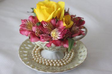 a white cup with flowers in it on a saucer next to a pearl bead necklace