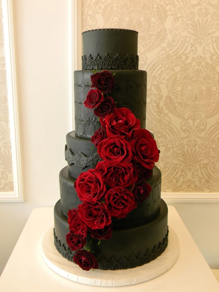 a three tiered black and red wedding cake with roses on it's side