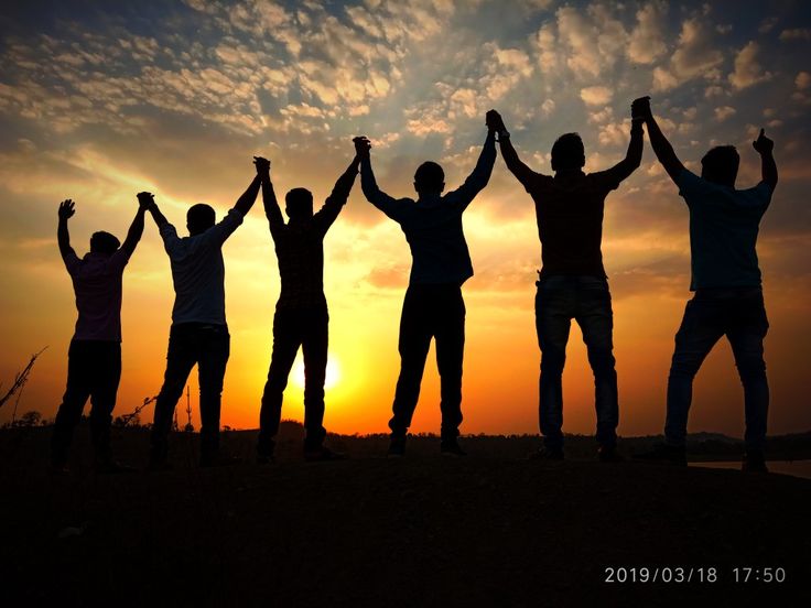 four people standing in the sunset with their arms up and hands raised above their heads