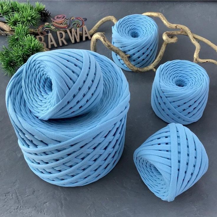 three blue yarns are sitting next to some pine branches