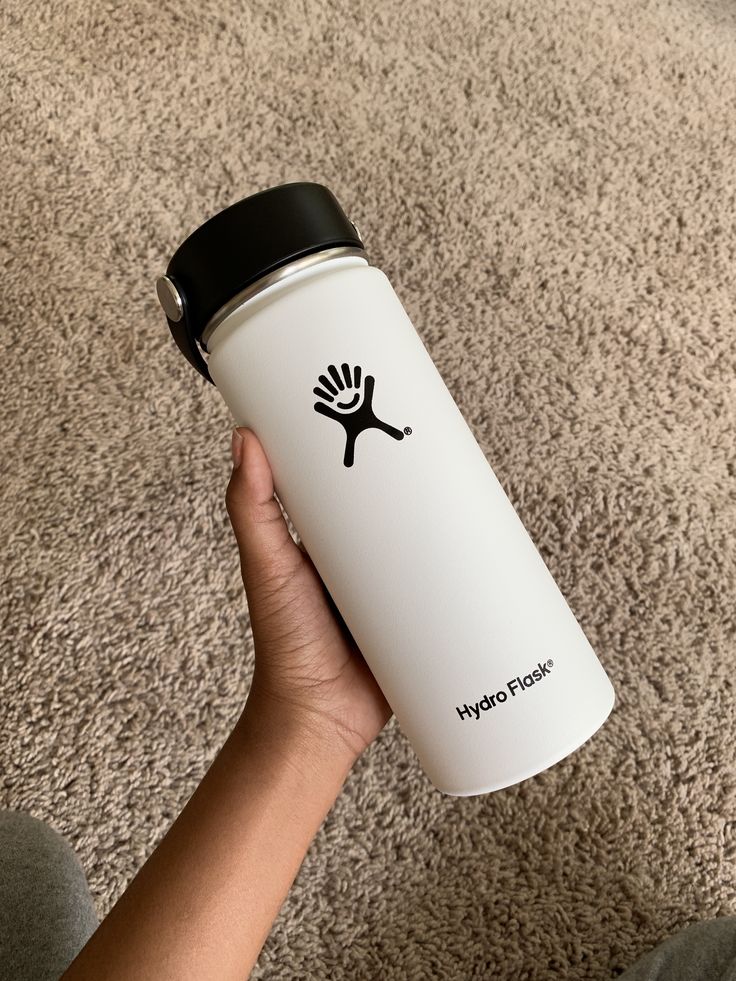 a hand holding a white water bottle with a black lid on carpeted room floor