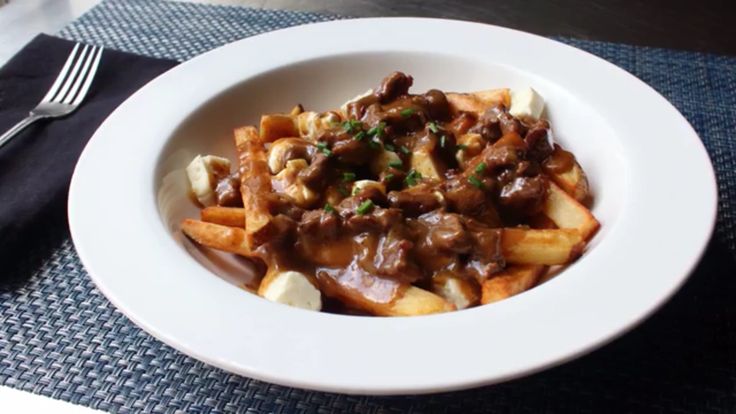 a white plate topped with french fries covered in gravy and meat toppings