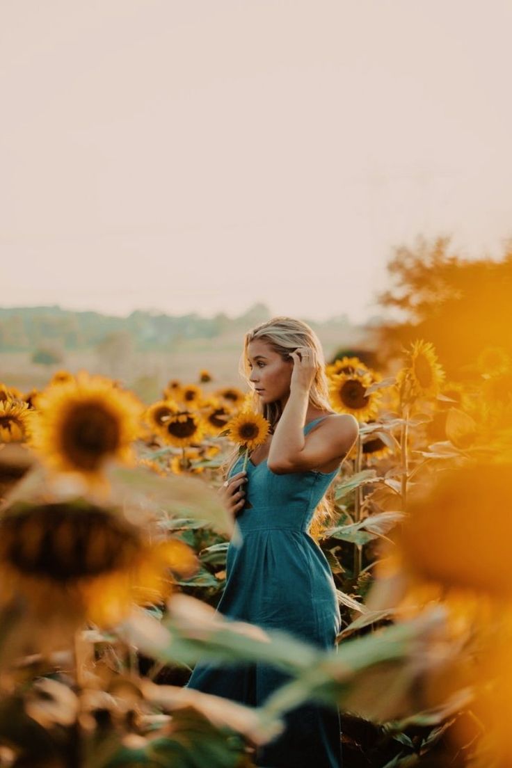 a woman standing in a field of sunflowers with her hand on her head