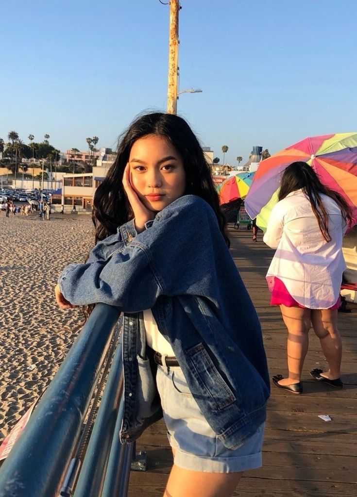 a woman standing on the beach with an umbrella in her hand and looking at the camera