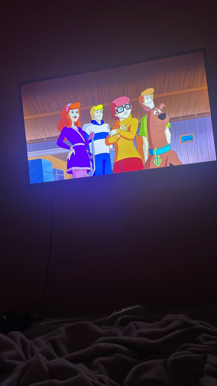 a television screen with cartoon characters on it's display in a dark room next to a bed