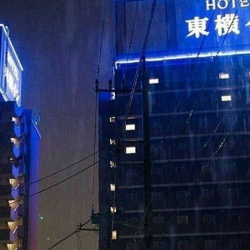 a city street at night in the rain with buildings lit up and signs on it