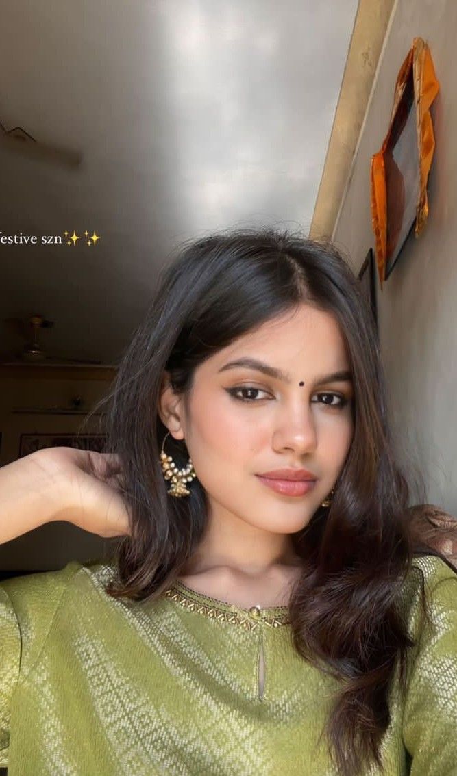 a woman with long dark hair wearing a green blouse and gold earrings, posing for the camera