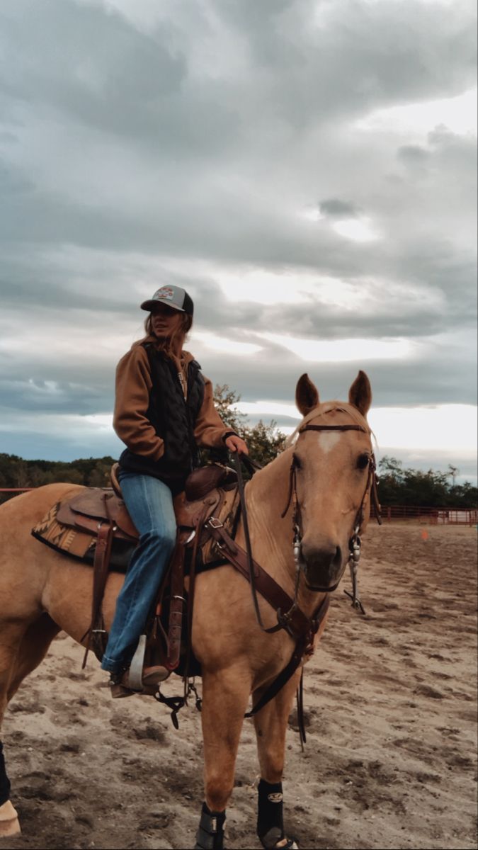 a man riding on the back of a brown horse in an open field under a cloudy sky