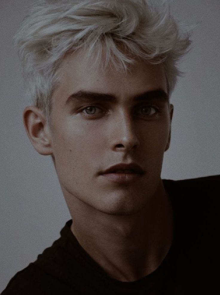 a man with white hair and blue eyes wearing a black t - shirt is looking at the camera