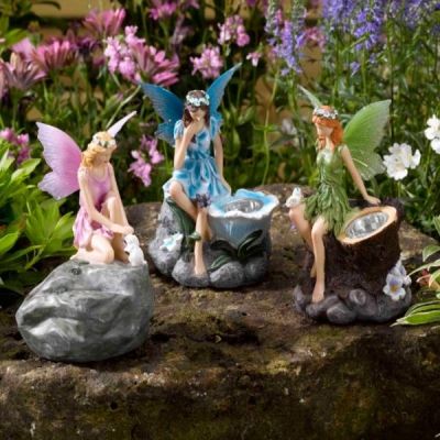 three little fairy figurines sitting on top of a rock with flowers in the background