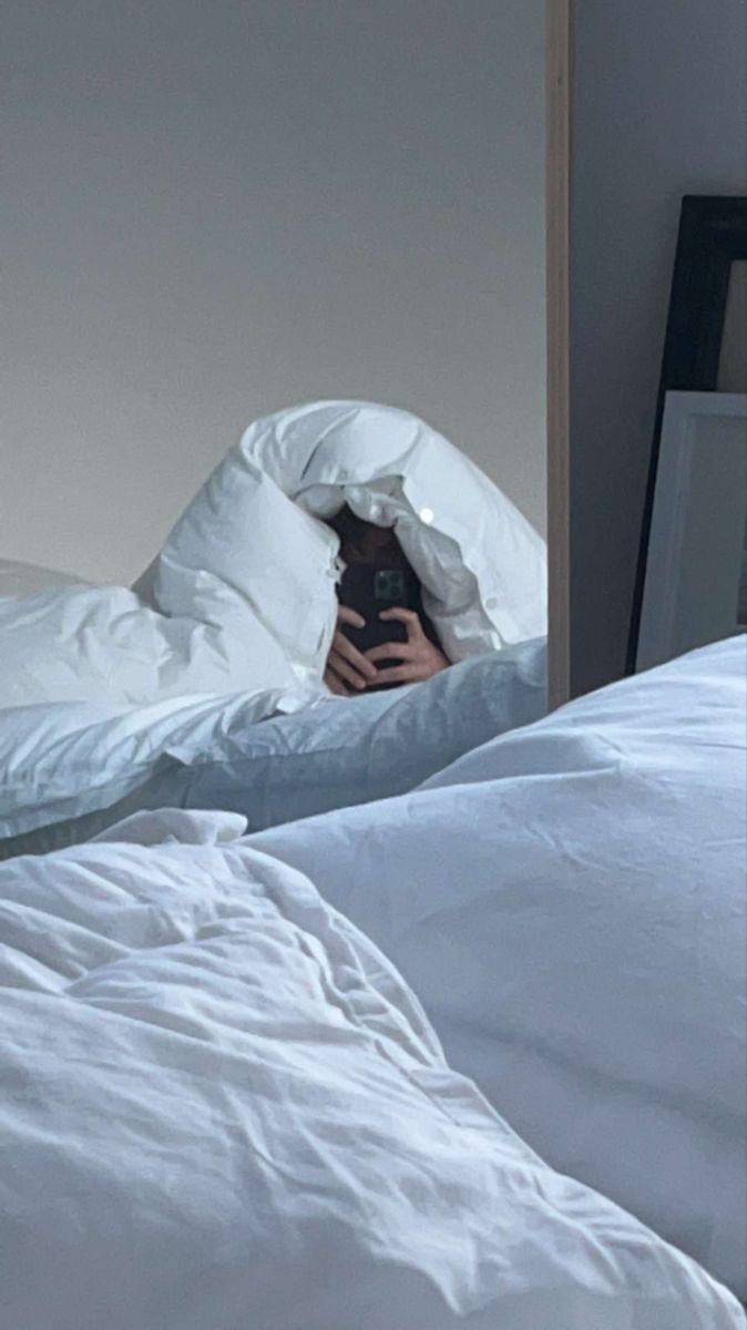 a person taking a selfie in bed with white sheets